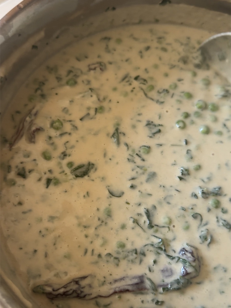 Creamy high-protein methi matar malai in a steel pan - green peas and chopped fenugreek leaves in a pale cottage cheese gravy, with whole dried red chilies on top.